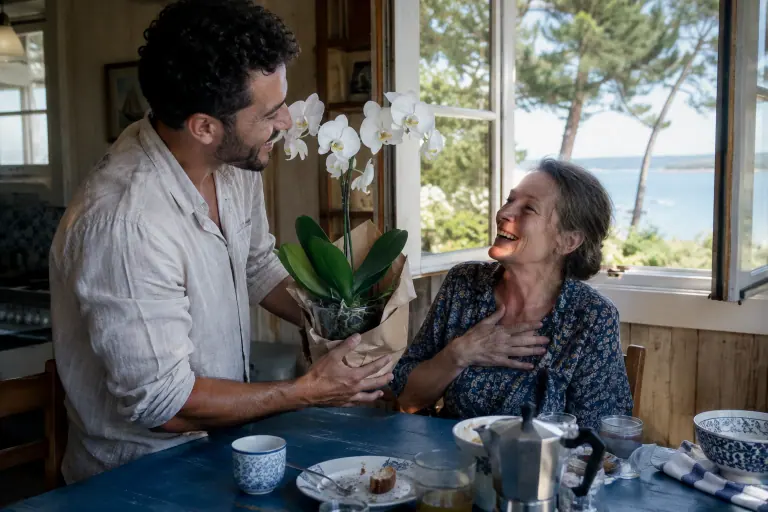 Dans une maison du bassin d’Arcachon, un homme offre à sa mère un phalaenopsis blanc à deux hampes, enveloppé de papier kraft